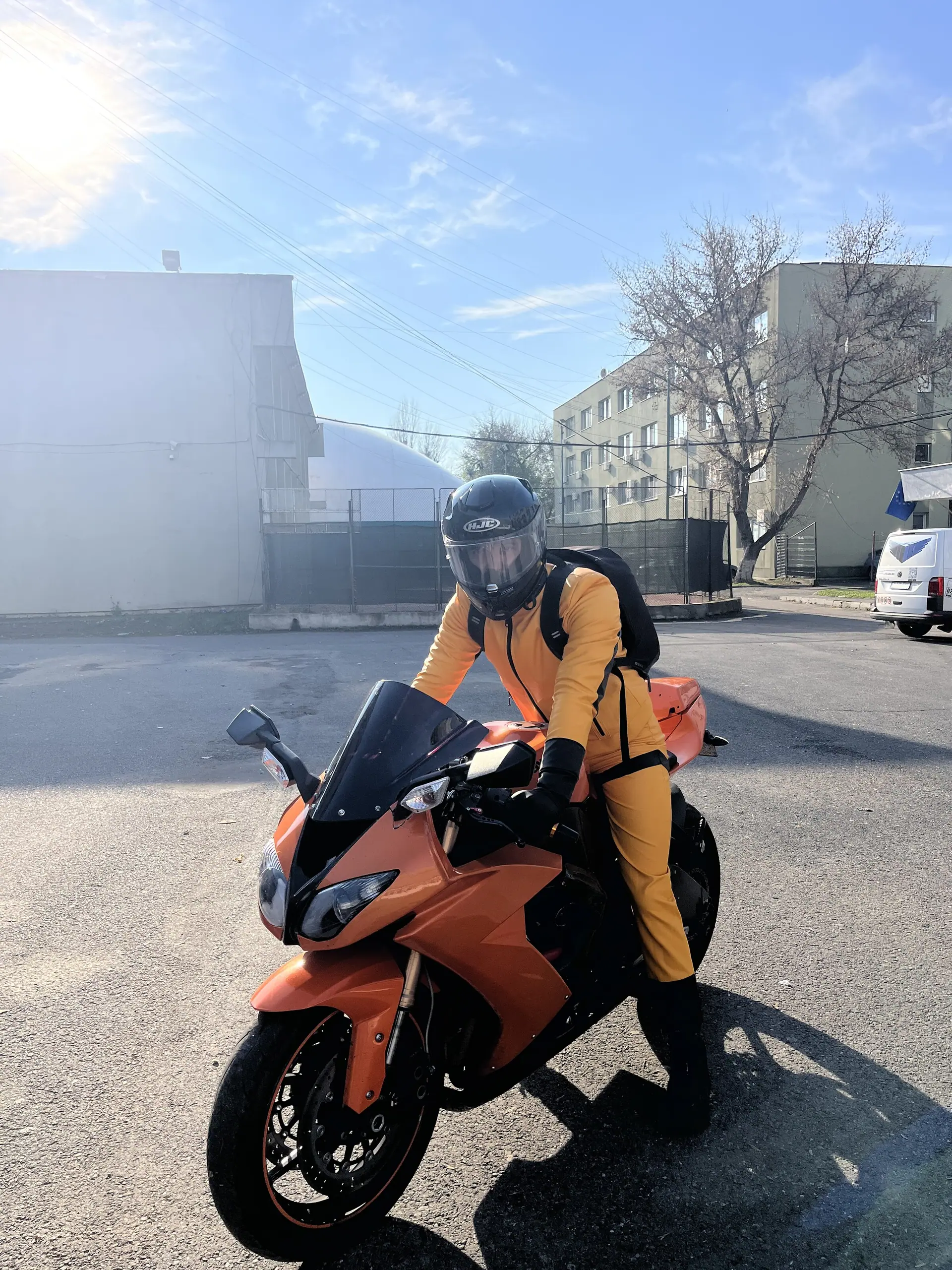 A biker character in orange and black leather, in a Bucharest school yard, posing with students and revving an engine.