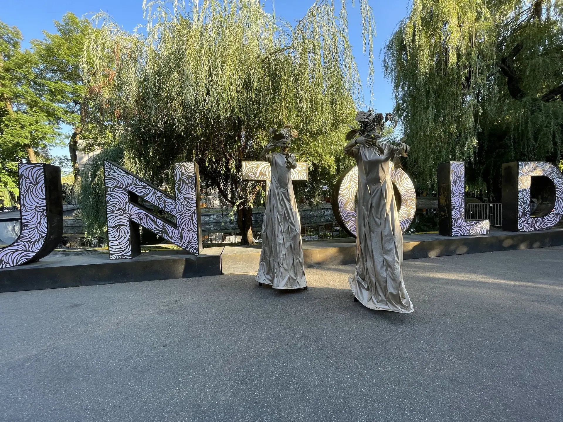 Stilt artists in white robes at the UNTOLD arch, and four Venetian-masked characters dancing beside Claptone.